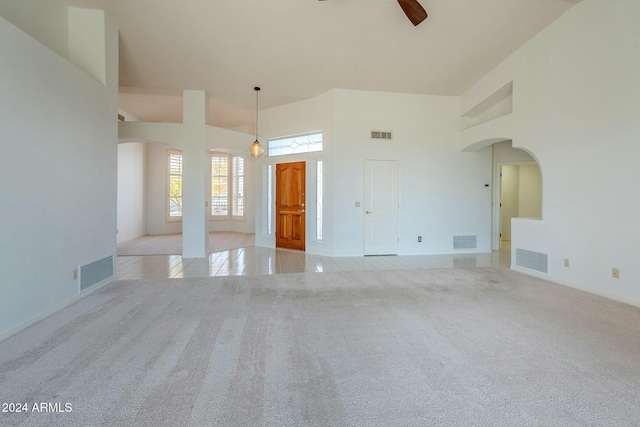 unfurnished living room featuring light carpet, a towering ceiling, and ceiling fan