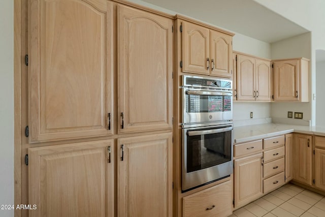 kitchen with light brown cabinetry, stainless steel double oven, and light tile patterned floors