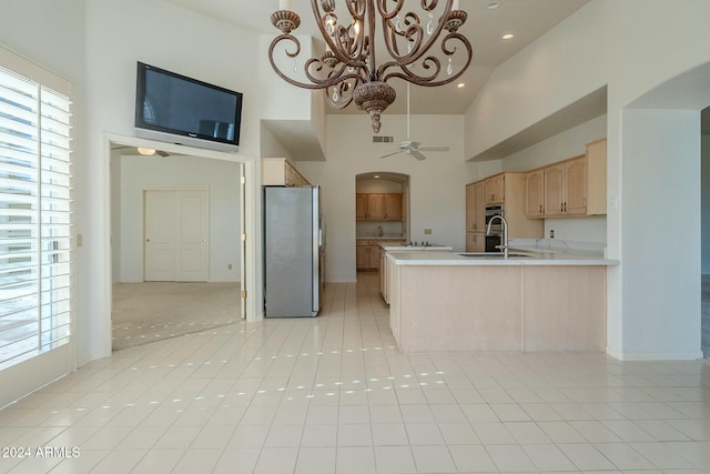 kitchen with light brown cabinets, high vaulted ceiling, light tile patterned floors, kitchen peninsula, and stainless steel refrigerator