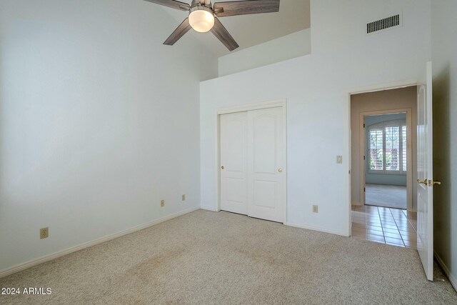 unfurnished bedroom featuring ceiling fan, a towering ceiling, light carpet, and a closet