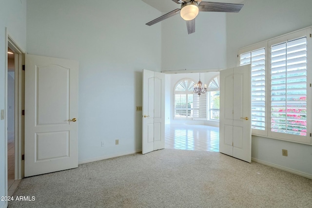 unfurnished room with a high ceiling, light colored carpet, and ceiling fan with notable chandelier