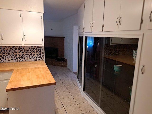 kitchen featuring decorative backsplash, light tile patterned floors, butcher block counters, white cabinets, and a brick fireplace