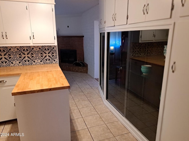 kitchen with wooden counters, light tile patterned floors, backsplash, white cabinetry, and a brick fireplace
