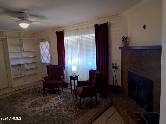 sitting room featuring a ceiling fan, a brick fireplace, and tile patterned floors