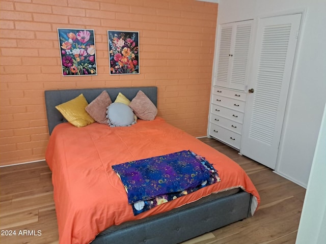 bedroom with brick wall, baseboards, wood finished floors, and a closet