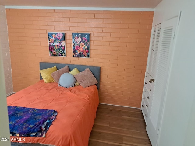 bedroom featuring brick wall and dark wood-type flooring