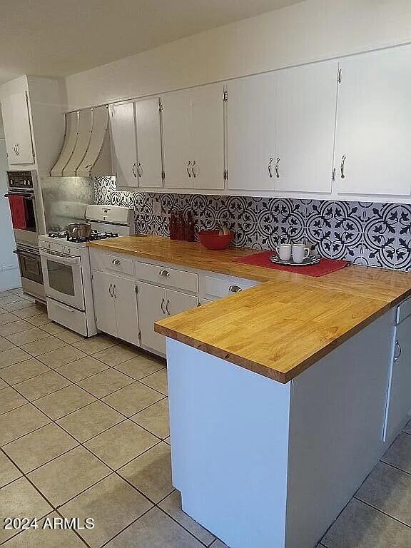 kitchen featuring light tile patterned floors, ventilation hood, tasteful backsplash, and gas range gas stove
