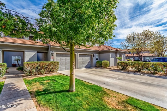 townhome / multi-family property with a front yard, concrete driveway, a tiled roof, and stucco siding