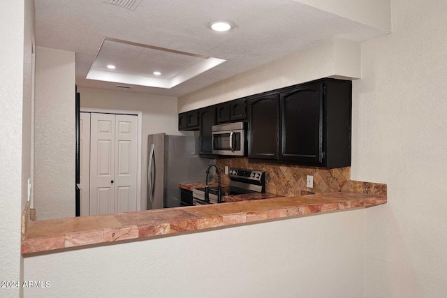 kitchen with tasteful backsplash, recessed lighting, a raised ceiling, appliances with stainless steel finishes, and dark cabinetry