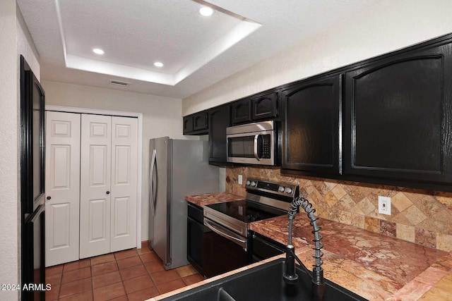 kitchen featuring tasteful backsplash, a raised ceiling, dark cabinets, tile patterned floors, and stainless steel appliances