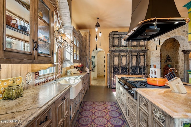 kitchen with sink, stainless steel gas stovetop, island range hood, and light stone countertops