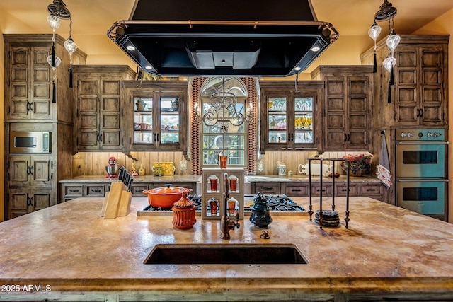 kitchen featuring double oven, exhaust hood, wooden walls, and a spacious island