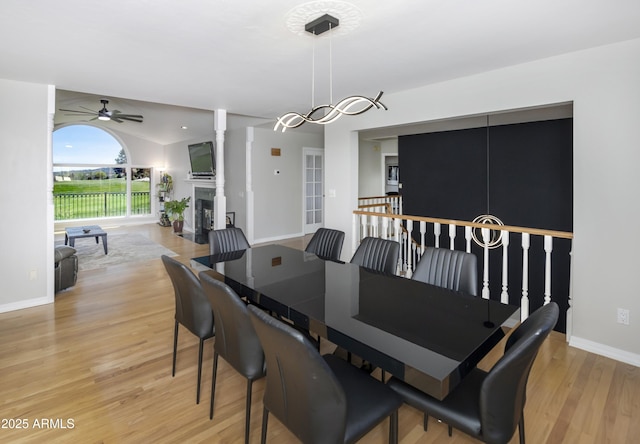 dining space featuring a ceiling fan, baseboards, light wood-style flooring, and a fireplace