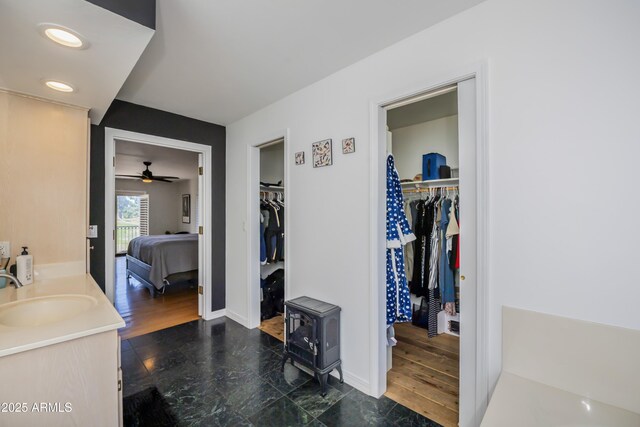 bathroom with a walk in closet, a wood stove, vanity, a ceiling fan, and baseboards