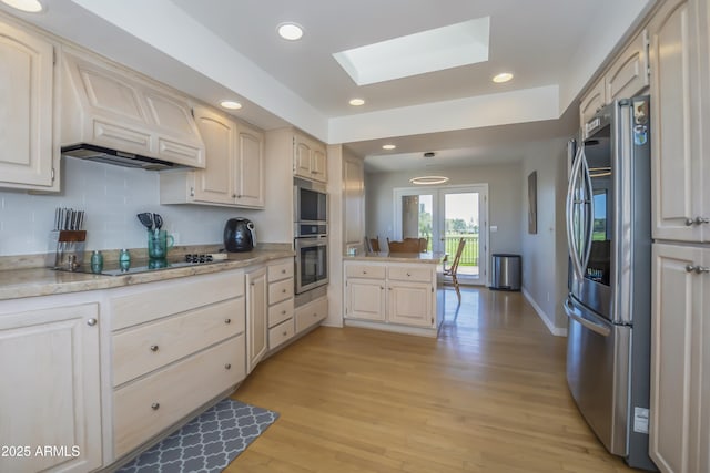 kitchen featuring backsplash, a skylight, appliances with stainless steel finishes, light wood-type flooring, and a peninsula