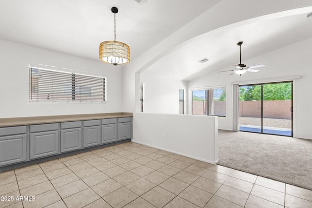 unfurnished room with a ceiling fan, visible vents, light colored carpet, vaulted ceiling, and light tile patterned floors