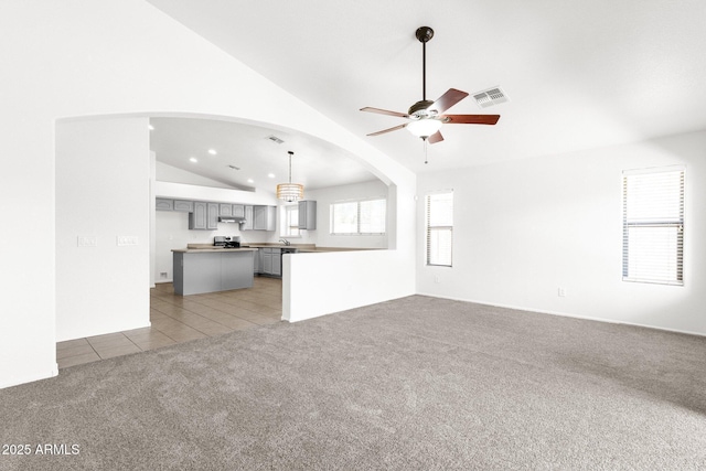 unfurnished living room with ceiling fan, visible vents, lofted ceiling, light carpet, and light tile patterned flooring
