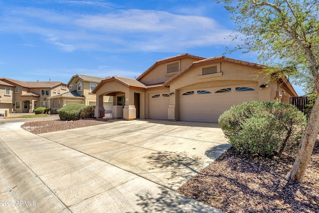 mediterranean / spanish home with a garage, stucco siding, a tiled roof, and concrete driveway