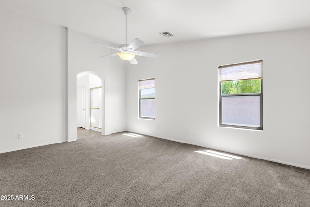 carpeted empty room with a healthy amount of sunlight, arched walkways, a ceiling fan, and visible vents