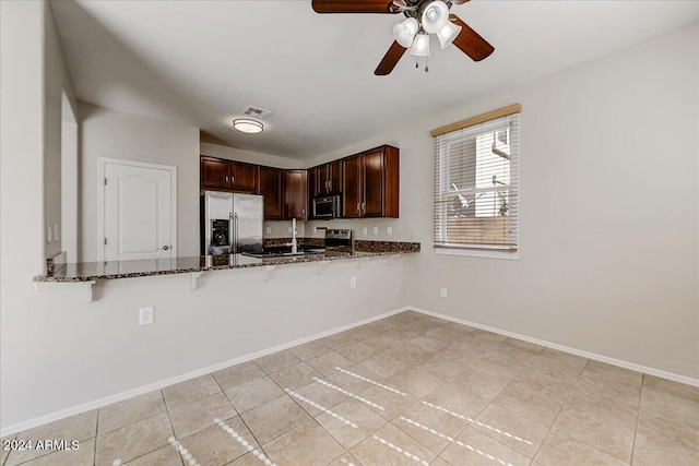 kitchen featuring kitchen peninsula, ceiling fan, appliances with stainless steel finishes, dark stone countertops, and light tile patterned flooring