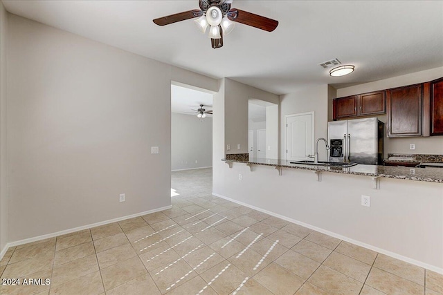 kitchen with dark stone countertops, sink, stainless steel fridge, light tile patterned flooring, and ceiling fan