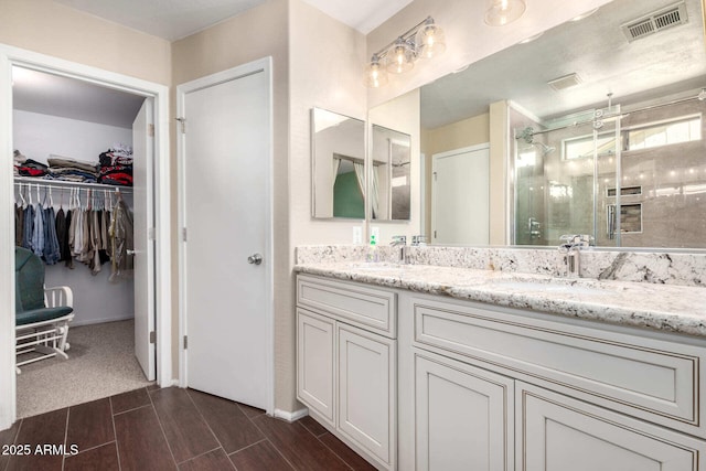 bathroom featuring double vanity, visible vents, wood tiled floor, a sink, and a shower stall