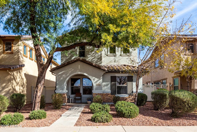 mediterranean / spanish home featuring stone siding, fence, stucco siding, and a tiled roof