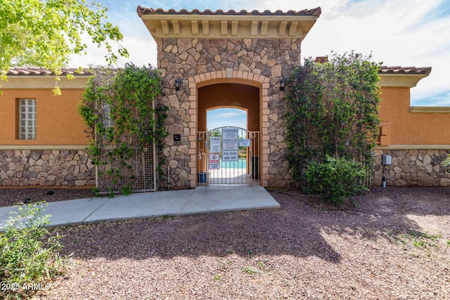 doorway to property with stone siding, fence, a gate, and stucco siding