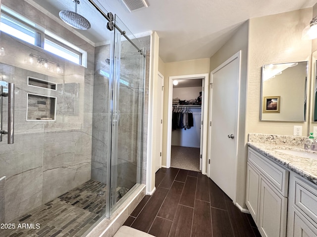 bathroom featuring vanity, visible vents, a shower stall, wood tiled floor, and a walk in closet