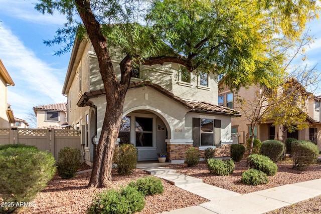 view of front of home with stone siding, fence, a tiled roof, and stucco siding