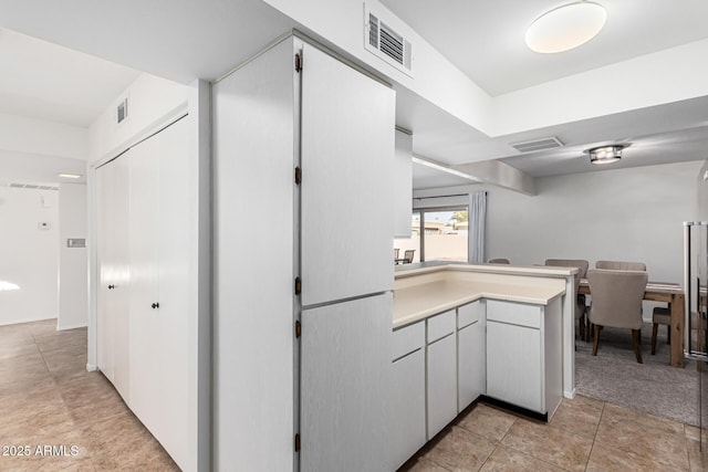 kitchen with light tile patterned floors, kitchen peninsula, and white cabinets