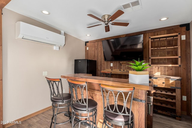 bar with ceiling fan, black refrigerator, hardwood / wood-style floors, wooden walls, and a wall mounted air conditioner