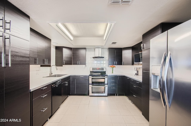 kitchen featuring backsplash, a raised ceiling, wall chimney range hood, sink, and appliances with stainless steel finishes