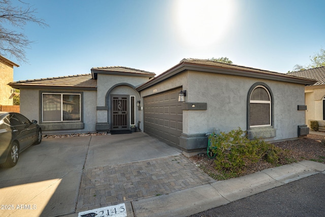 mediterranean / spanish-style home with a garage, driveway, a tiled roof, and stucco siding