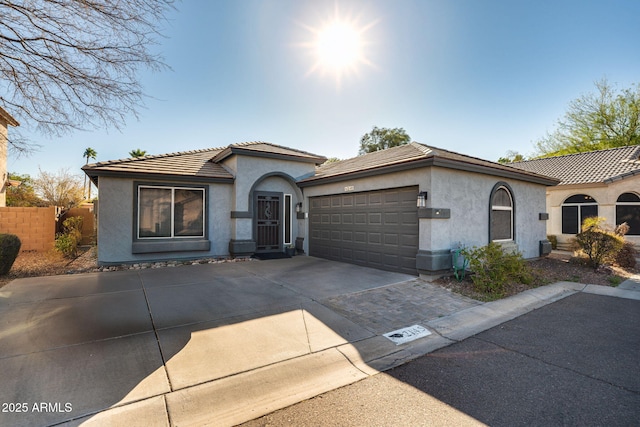 view of front of house with driveway, an attached garage, a tile roof, and stucco siding