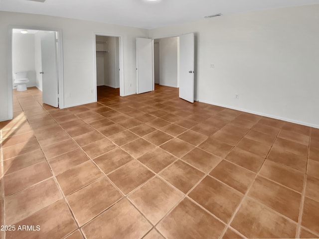 unfurnished bedroom featuring ensuite bath, a spacious closet, and tile patterned flooring