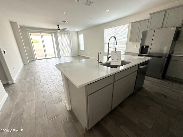 kitchen featuring ceiling fan, sink, stainless steel appliances, an island with sink, and light wood-type flooring