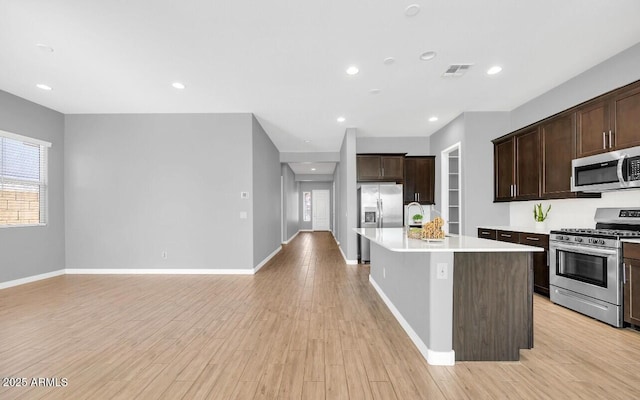 kitchen with dark brown cabinetry, stainless steel appliances, light hardwood / wood-style floors, and an island with sink