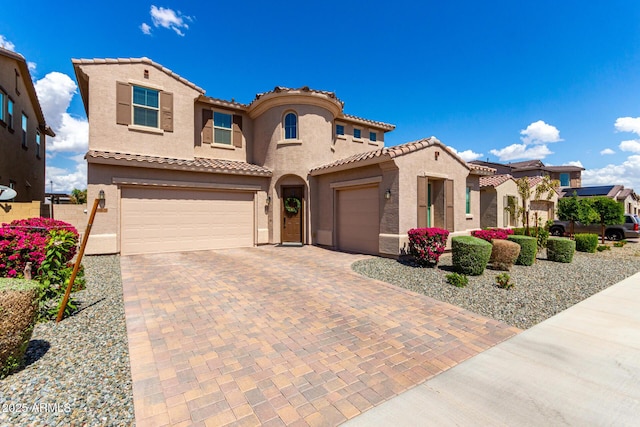 mediterranean / spanish house with a tiled roof, a garage, stucco siding, and decorative driveway