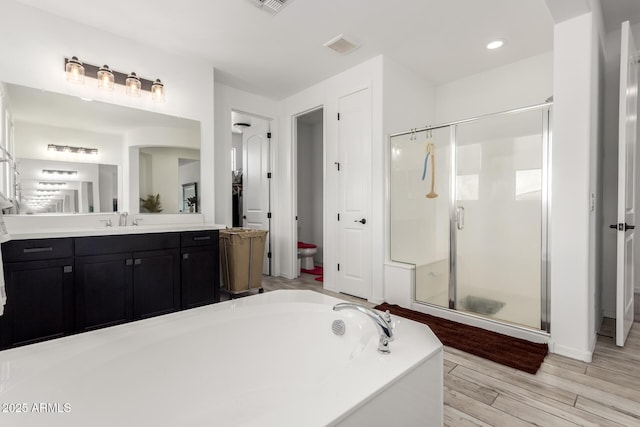 bathroom with a bath, a stall shower, wood finished floors, and vanity