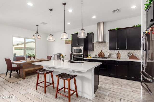 kitchen featuring tasteful backsplash, visible vents, wall chimney exhaust hood, a breakfast bar area, and stainless steel appliances