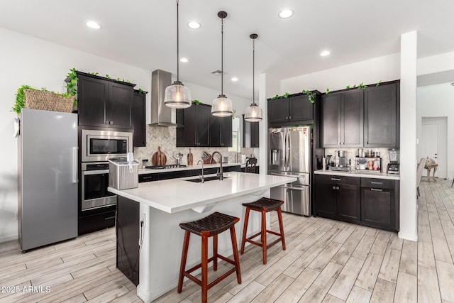 kitchen featuring wall chimney exhaust hood, a sink, light countertops, appliances with stainless steel finishes, and wood finish floors