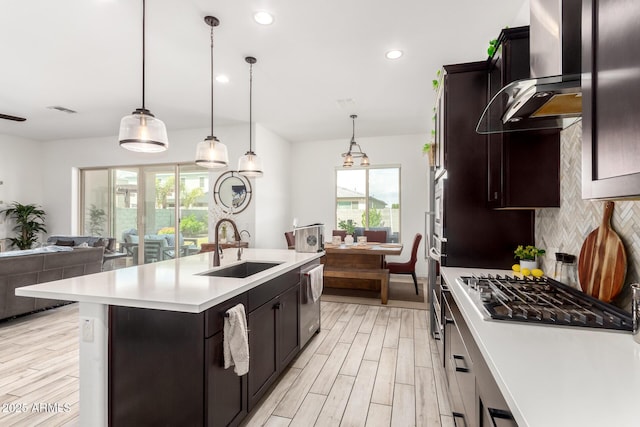 kitchen with a sink, wall chimney range hood, light countertops, stainless steel appliances, and decorative backsplash