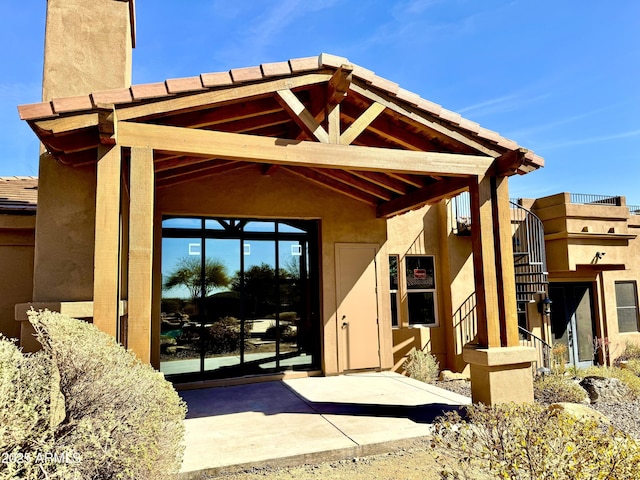 back of house featuring a patio, stairway, a chimney, and stucco siding