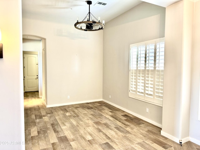 spare room featuring arched walkways, a chandelier, wood finished floors, visible vents, and baseboards