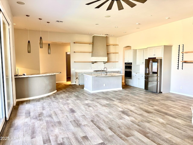 kitchen with open shelves, visible vents, appliances with stainless steel finishes, a sink, and wall chimney range hood