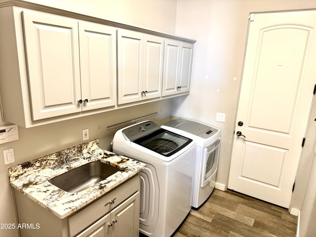 clothes washing area featuring a sink, cabinet space, separate washer and dryer, and light wood-style floors