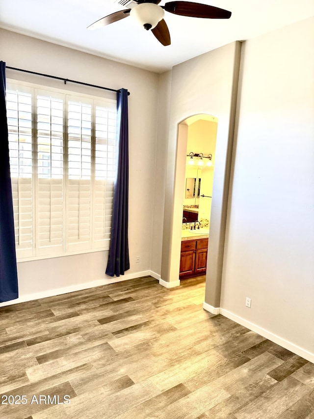 empty room with light wood-style floors, arched walkways, ceiling fan, and baseboards