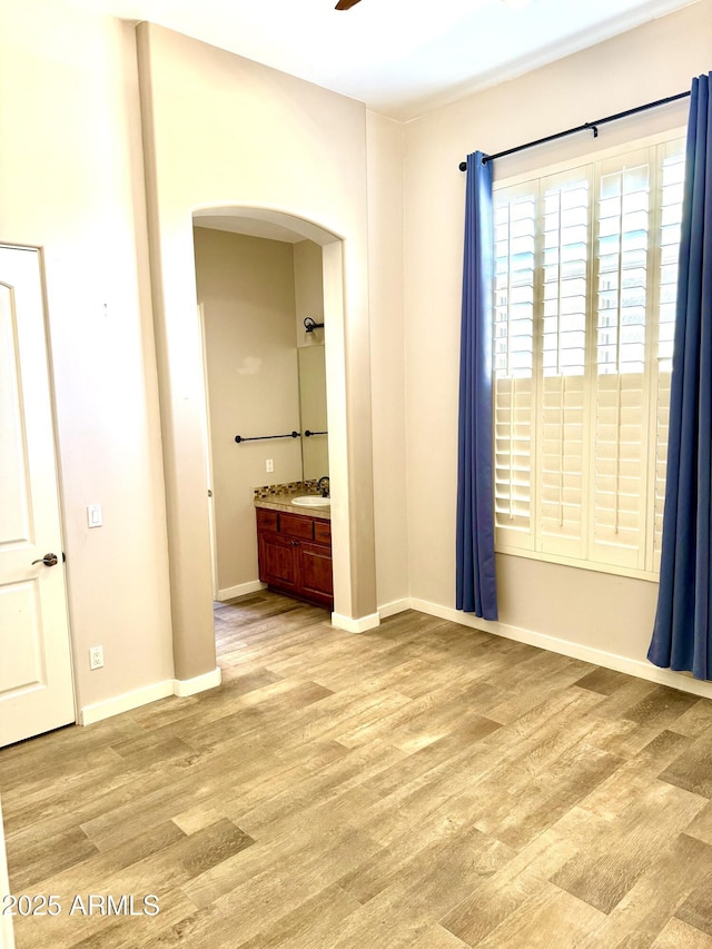 unfurnished bedroom with light wood-style floors, a sink, baseboards, and ensuite bathroom