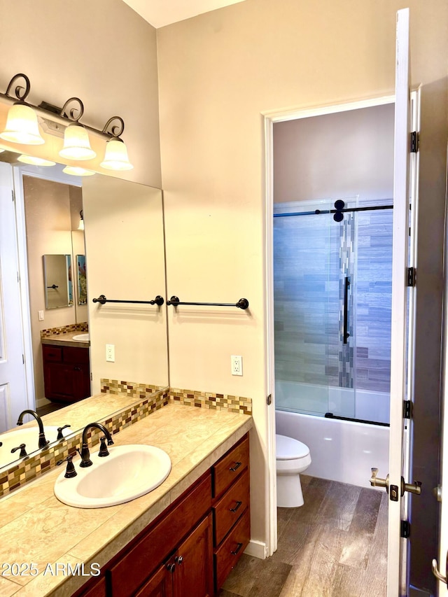 bathroom with tasteful backsplash, toilet, enclosed tub / shower combo, wood finished floors, and vanity